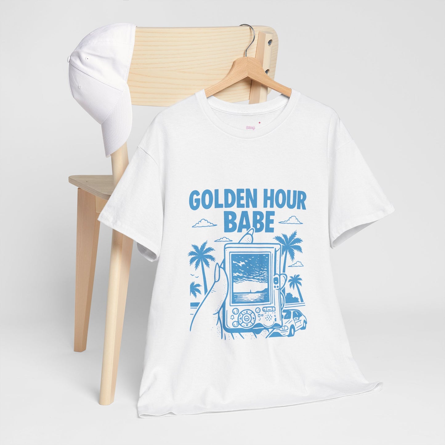 White t-shirt with 'GOLDEN HOUR BABE' design on a wooden chair against a white background