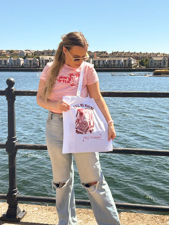 Person holding a tote bag by a waterfront with houses in the background