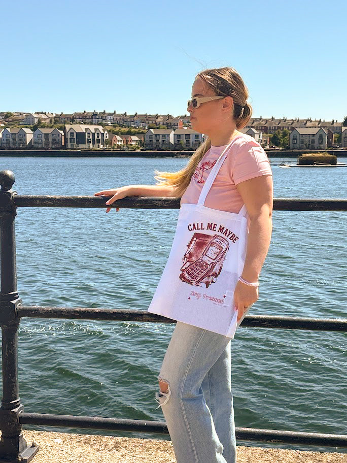 Person holding a 'Call Me Maybe' apron by the water