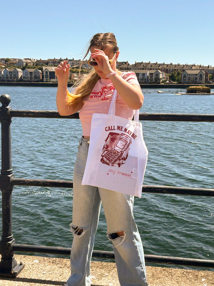 Person holding a tote bag with text by a waterfront