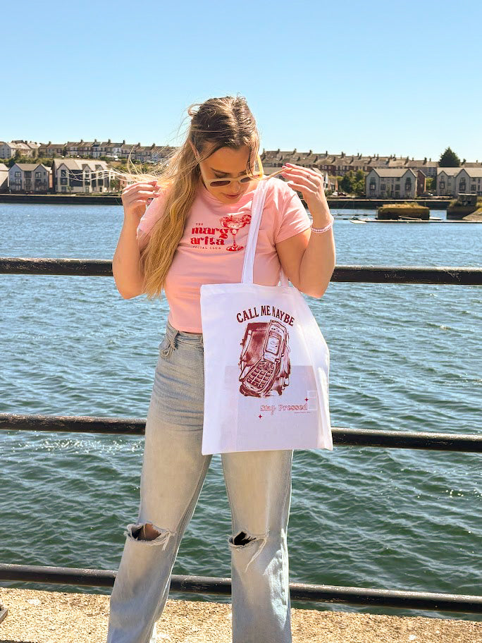 Person holding a white tote bag with red text by a waterfront