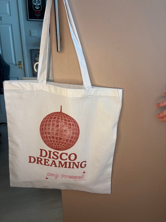 Tote bag with 'Disco Dreaming' design hanging on a door