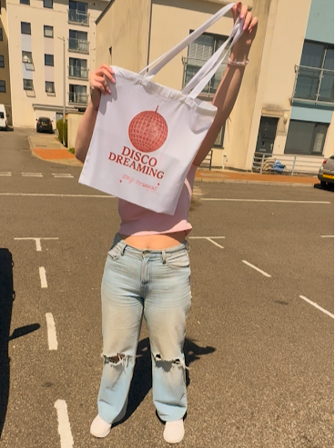 Person holding a tote bag with 'Disco Dreaming' text in an urban setting