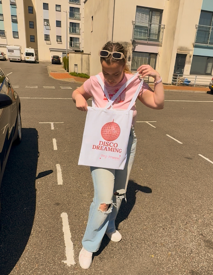 Person holding a tote bag with 'Disco Dreaming' text on a street.