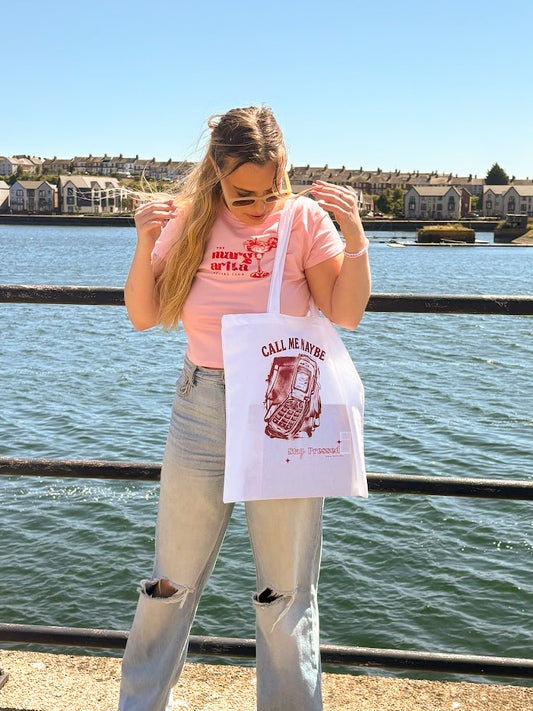 Person holding a white tote bag with red text by a waterfront